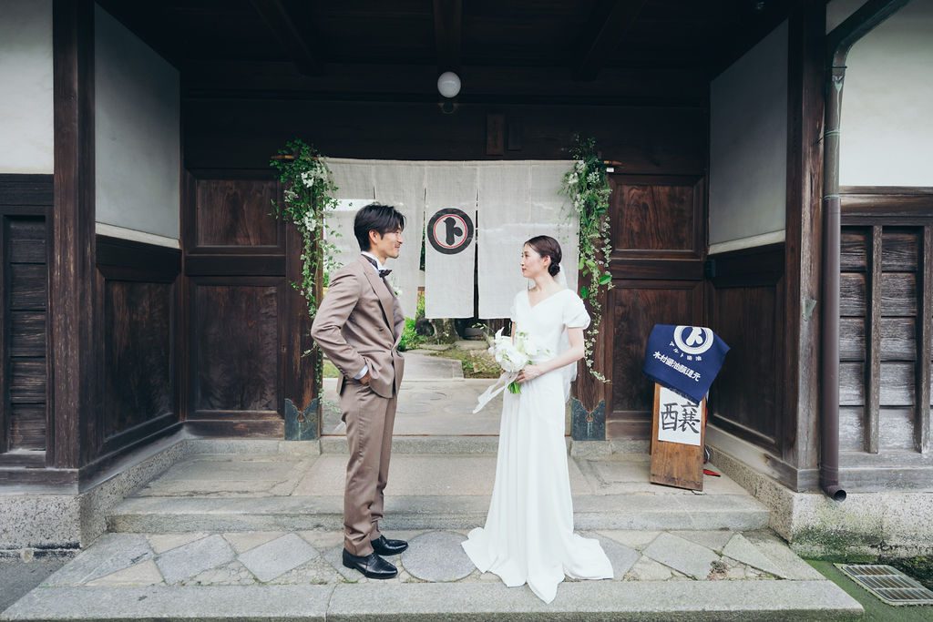 醤油蔵の暖簾の前で向かい合う新郎新婦